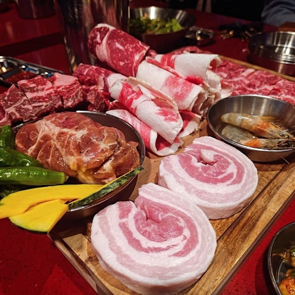 Assortment of raw Korean BBQ meats, including sliced pork belly, beef, and marinated pork, with vegetables and shrimp.