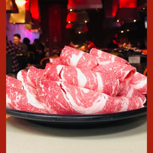 Platter of thinly sliced, marbled beef for Korean BBQ, with a blurred restaurant background.