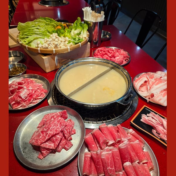 A Korean BBQ table with a hot pot, various cuts of raw meat, and a basket of fresh vegetables.