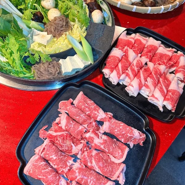 Plates of thinly sliced raw beef and a hot pot with vegetables, tofu, and noodles for Korean BBQ.