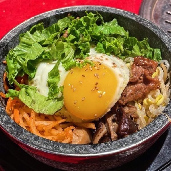 A stone bowl of Moodaepo Korean BBQ bibimbap with a fried egg, lettuce, and various vegetables.