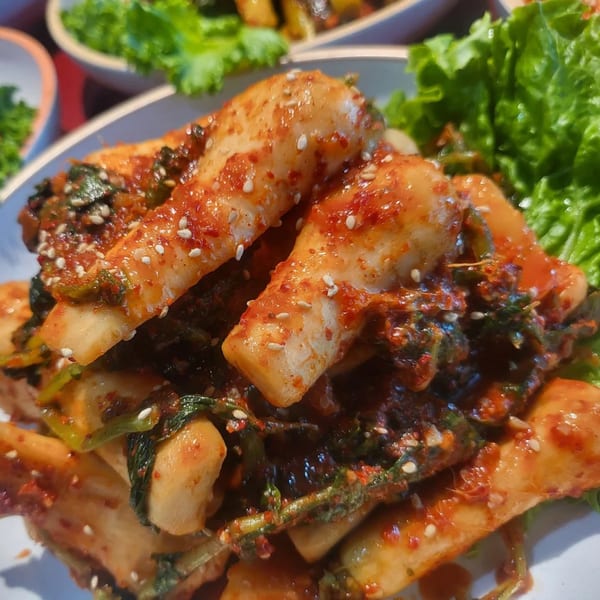 Spicy Korean radish kimchi (Kkakdugi) with sesame seeds and fresh lettuce on a white plate.